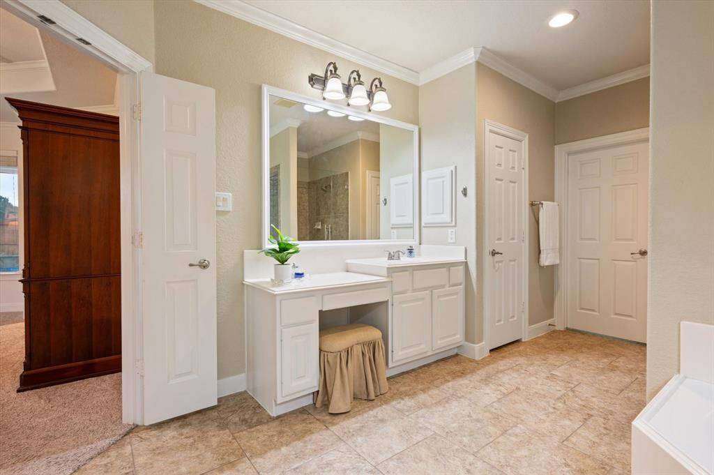 Dual vanities with granite countertops offer ample space for morning routines, each adorned with framed mirrors and elegant vanity lighting for a polished, refined look. A dedicated sit-down vanity area adds an extra layer of comfort and convenience.