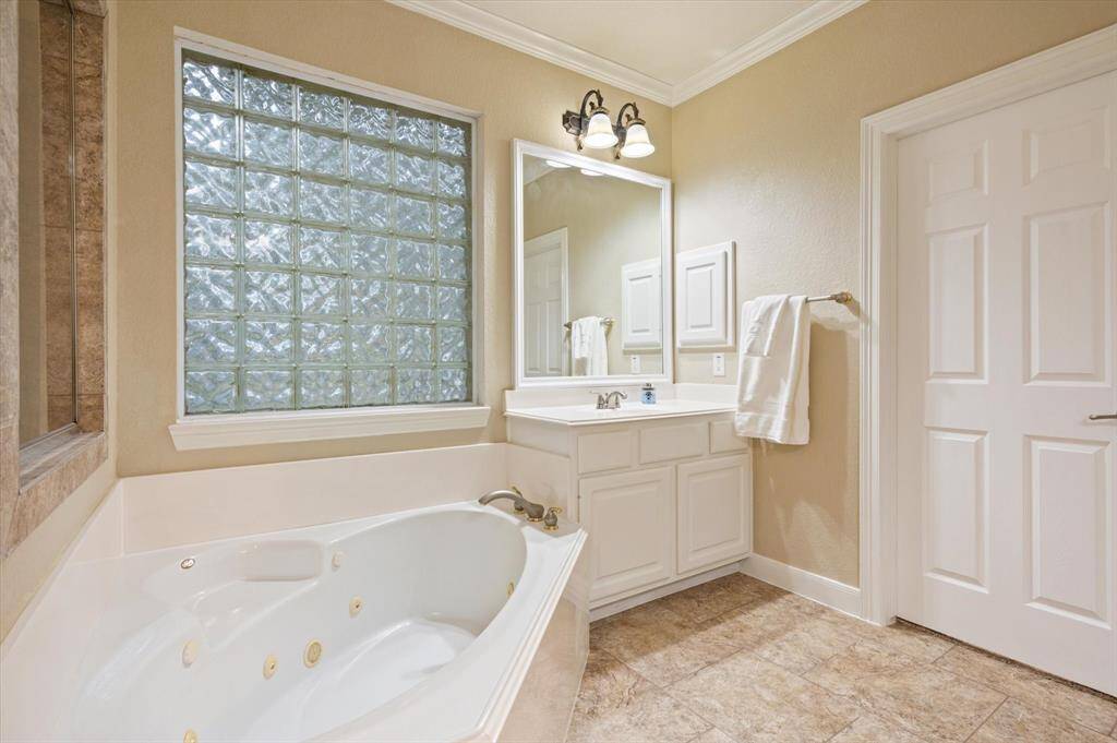 A deep soaking tub with jets invites you to unwind, perfectly positioned beneath a large frosted glass block window that fills the room with soft, diffused light while preserving your privacy.
