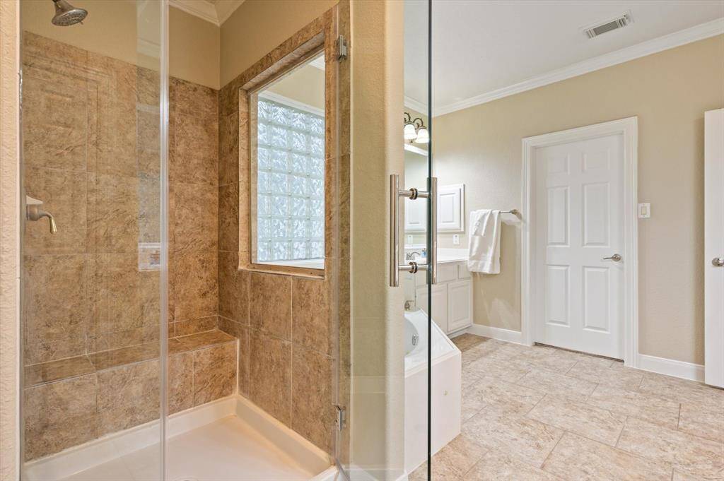 The spacious walk-in shower features a sleek, frameless glass enclosure that creates a clean, modern aesthetic and an open, airy feel. Along the back wall, a built-in bench offers a comfortable spot to sit and unwind, allowing you to relax as warm water cascades gently around you.