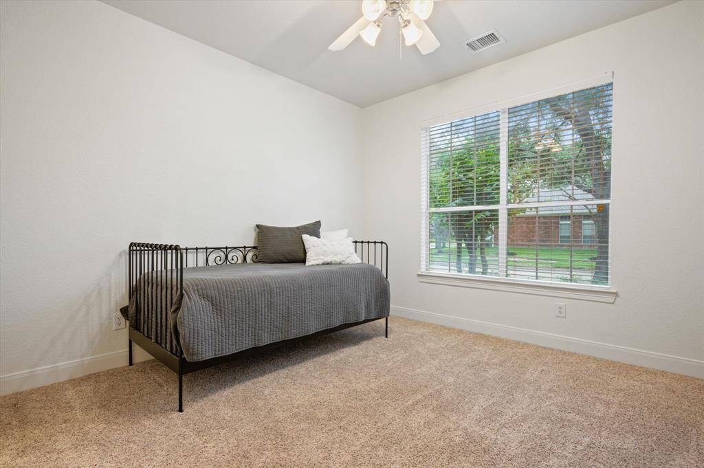 This first-floor secondary bedroom features plush carpet, a high ceiling with a fan, and a large front-facing window. It also offers direct access to a full bathroom—ideal for guests or extended family.
