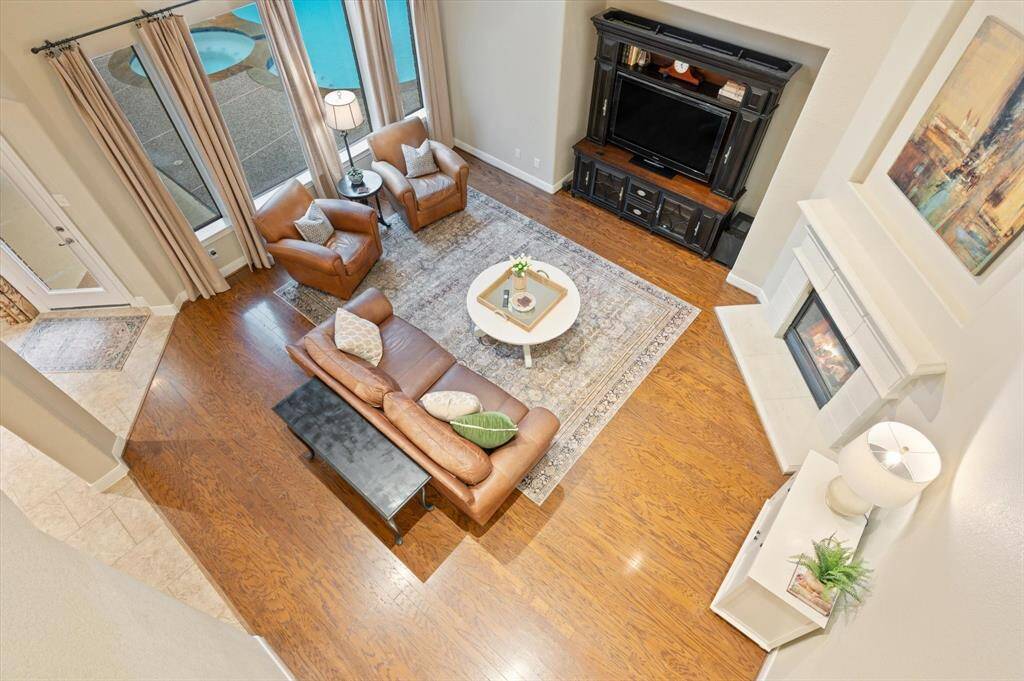 The spacious family room is beautifully showcased from the second-floor landing, offering a clear view of its open layout, abundant natural light streaming through the large windows, and the inviting warmth of the gas-log fireplace framed by an elegant cast stone surround.