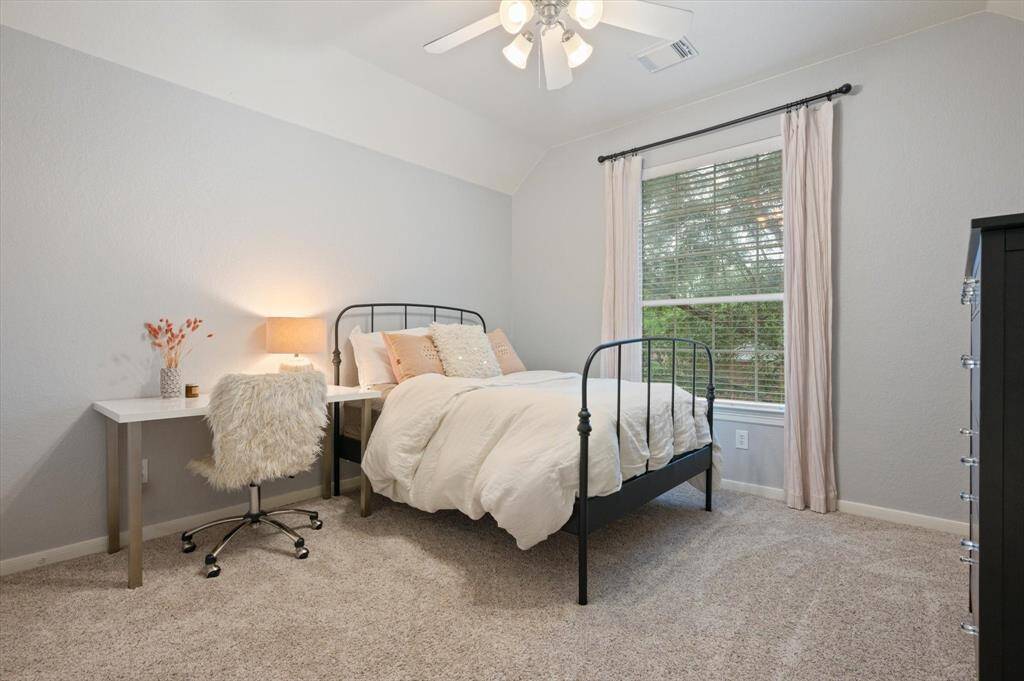 This spacious upstairs secondary bedroom features a high ceiling with a ceiling fan, plush carpeting, and a large window that fills the room with natural light. It also offers the convenience of direct access to a full bathroom, making it an ideal space for comfort and privacy.