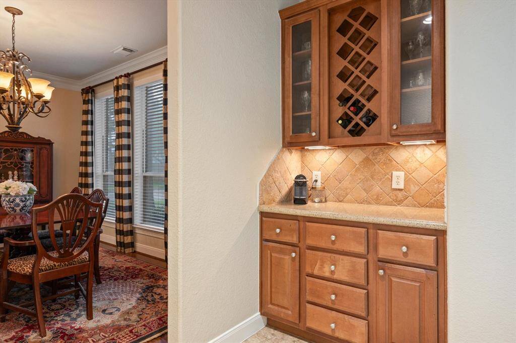 Perfectly positioned between the formal dining room and kitchen, the butler’s pantry offers a wall of cabinets and drawers topped with sleek granite countertops and a stone tile backsplash. Above, glass-front cabinets and a built-in wine rack provide elegant storage.