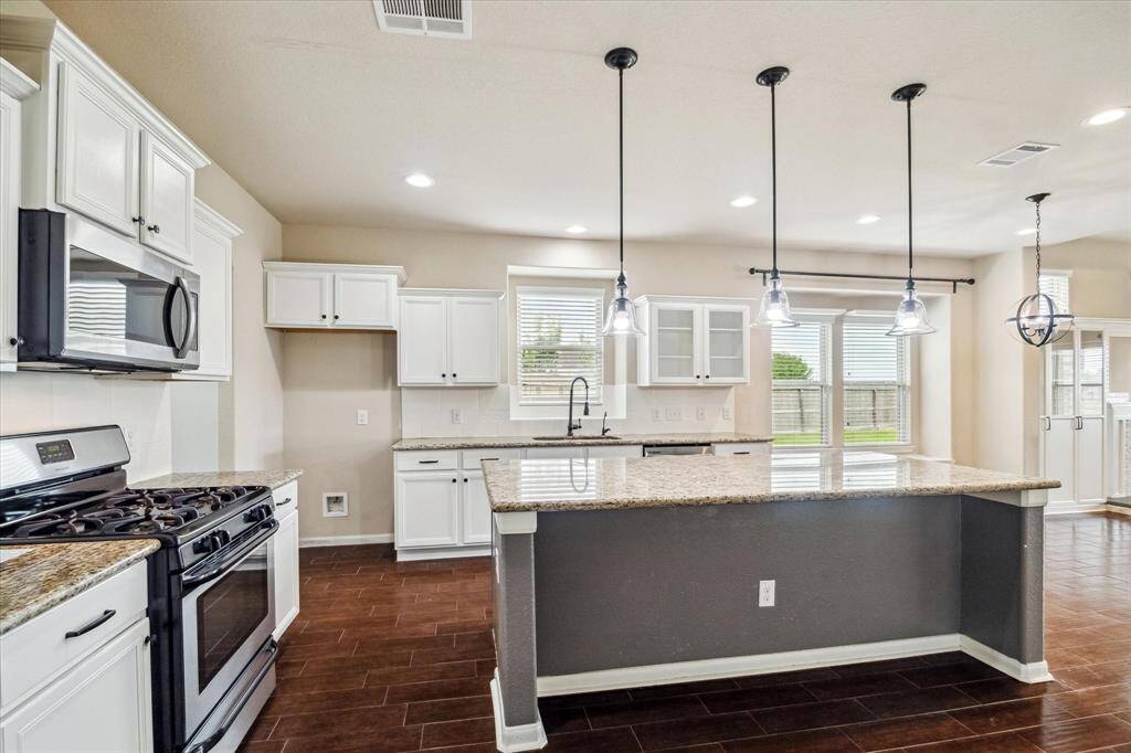 This fully loaded island kitchen is the heart of the home, featuring granite countertops, crisp white cabinetry with modern hardware, and sleek stainless steel appliances. Pendant lighting highlights the expansive island, perfect for meal prep, casual dining, or gathering with friends and family.