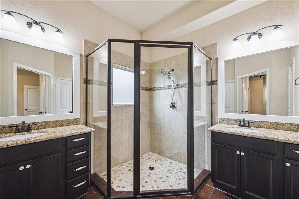 The owner's ensuite blends style and function with dual granite-topped vanities, framed mirrors, and oil-rubbed bronze fixtures. A spacious walk-in shower takes center stage, showcasing floor-to-ceiling tile, a mosaic tile floor, built-in seating, and a privacy window that fills the space with natural light.