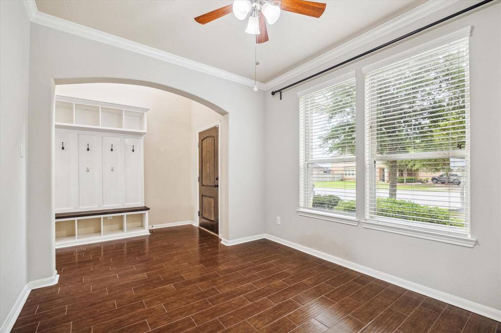 This versatile space near the entry is ideal for a home office, formal living, or formal dining with rich wood-look tile flooring, elegant crown molding, and abundant natural light from large picture windows overlooking the front yard.