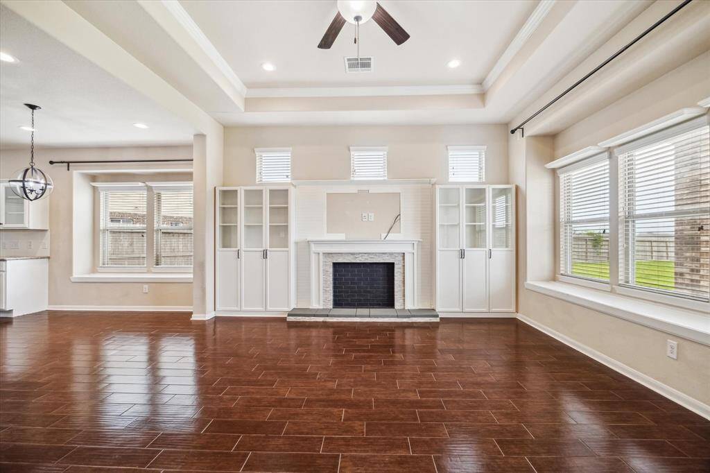Built-in cabinetry adds both function and style to this elegant family room, flanking a striking mock fireplace that serves as the focal point of the space. With rich wood-look tile flooring, a tray ceiling with crown molding, and plenty of natural light, this room is the perfect blend of comfort and sophistication.