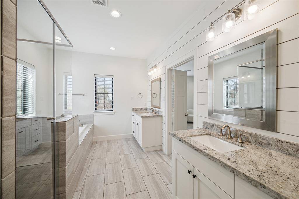 Spa-like primary bath through double doors offers separate sink areas, soaking tub, and shiplap accent wall.