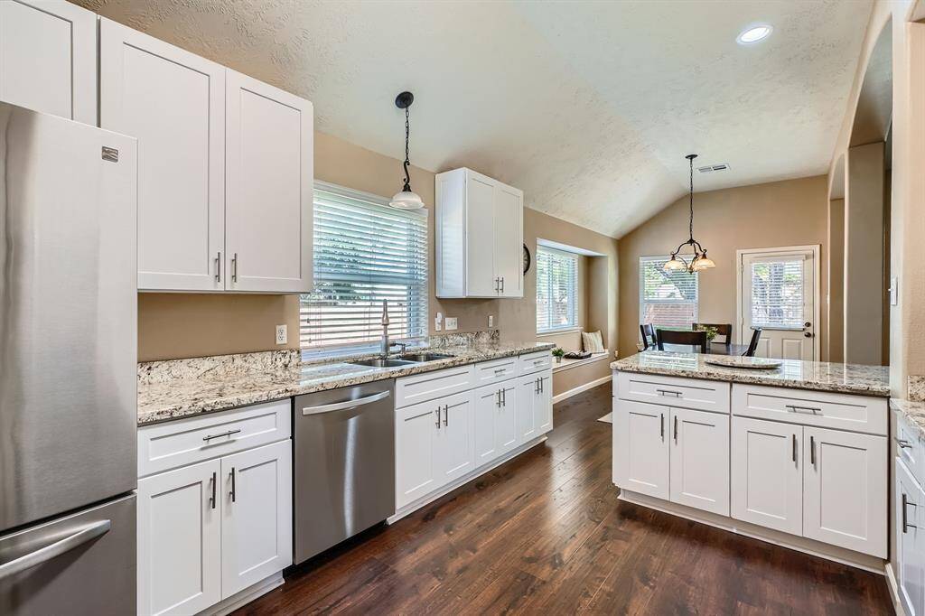 This kitchen features modern white cabinetry, granite countertops, and stainless steel appliances. The open layout includes a cozy dining area with large windows, offering plenty of natural light and a welcoming atmosphere.