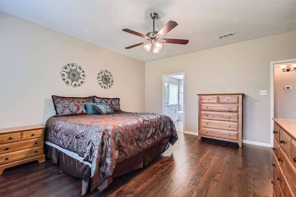 This inviting bedroom features  a ceiling fan, and neutral walls. It's suits a with a large bed and dressers, and it offers access to an ensuite bathroom.