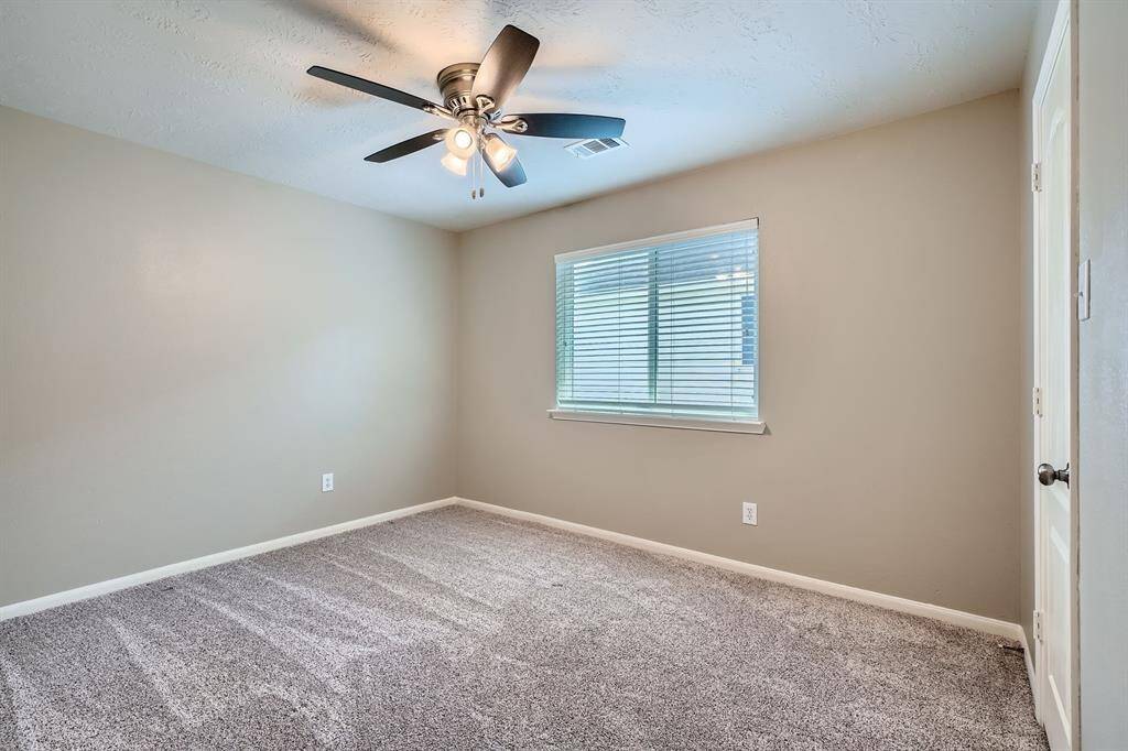 This room features neutral-colored walls, a plush carpet, and a ceiling fan with lights. A window with blinds allows natural light to fill the space, creating a bright and inviting atmosphere.