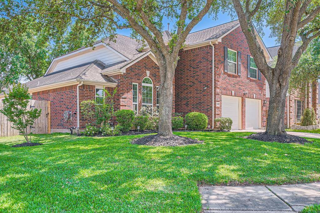 Charming two-story brick home with a well-maintained lawn and mature trees. Features a two-car garage, lush landscaping, and a welcoming front entrance. Ideal for family living in a serene neighborhood.