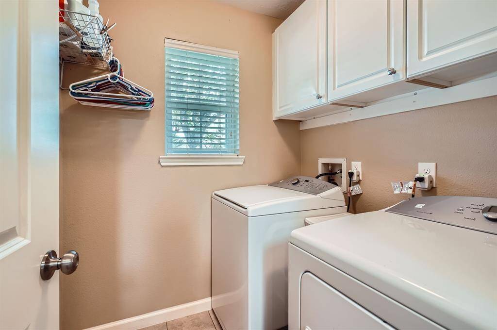 This is a well-lit laundry room featuring room for large washer and dryer set up, upper storage cabinets, and a small window for natural light.