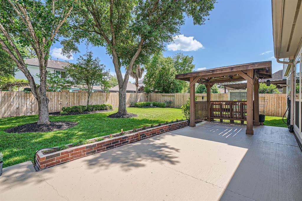 Spacious backyard featuring a well-maintained lawn, mature trees, a wooden pergola for shade, and a large patio area, perfect for outdoor gatherings.