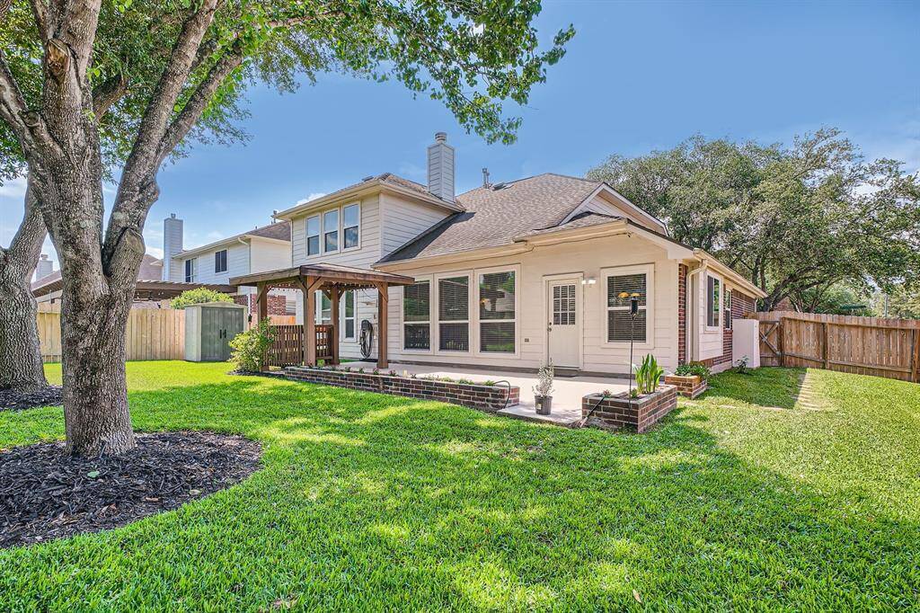 This property features a spacious backyard with lush green lawn, mature trees, and a charming covered patio area. The house exterior is well-maintained, offering a cozy and inviting atmosphere perfect for outdoor relaxation and entertainment.