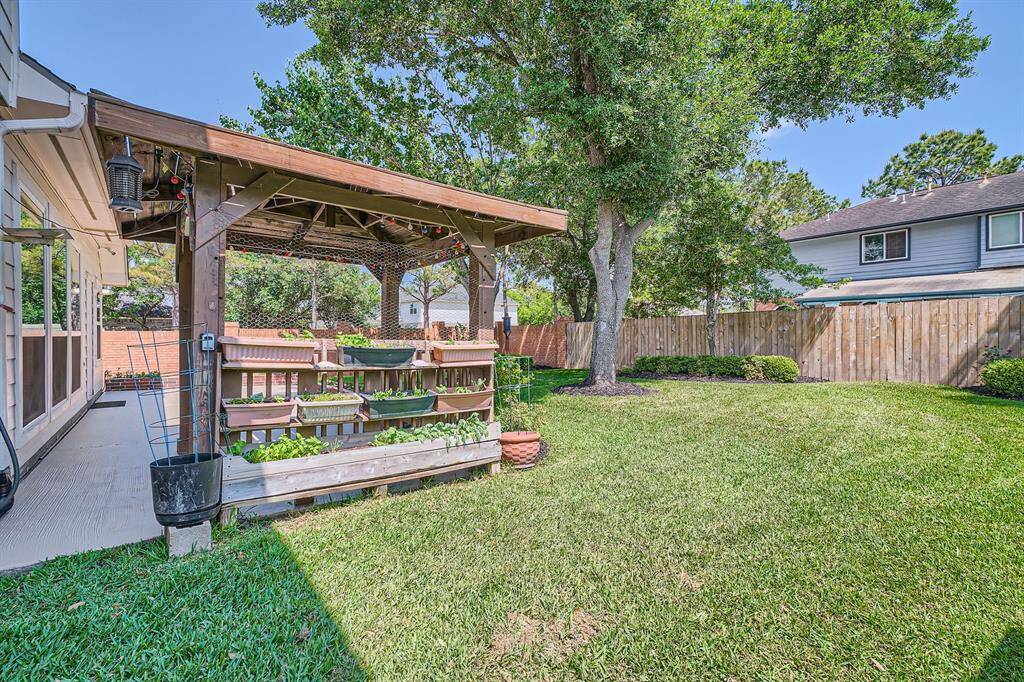 This backyard features a cozy pergola with planters for gardening, a well-maintained lawn, and mature trees, providing a relaxing and private outdoor space.