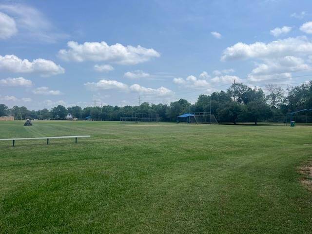 Wide open grassy field with a few trees and sports equipment under a blue sky with scattered clouds, perfect for outdoor activities.