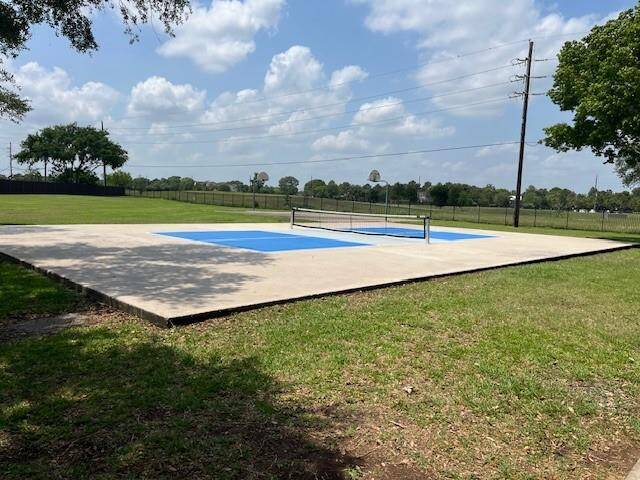 A spacious outdoor area featuring a pickleball court for the hottest exercise trend with a blue and white surface, surrounded by green grass and trees. It's ideal for sports enthusiasts and offers a serene, open setting for recreation.