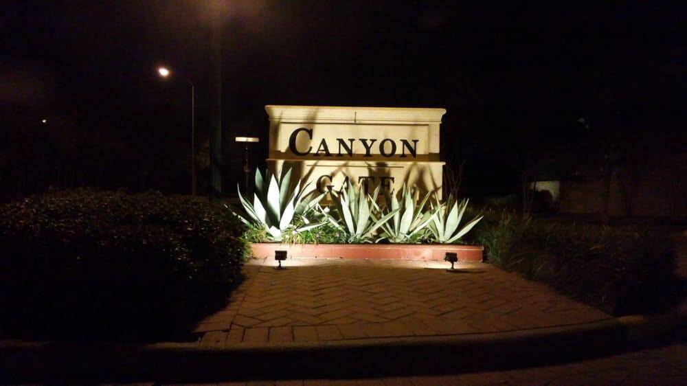 Entrance sign for "Canyon Gate" at night, surrounded by manicured landscaping with agave plants, creating a welcoming and upscale impression of the community.