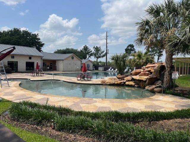 Public oasis with a large, resort-style pool featuring a waterfall and palm trees. The area includes a spacious patio with seating and umbrellas, surrounded by lush greenery. It's ideal for relaxation and entertaining.