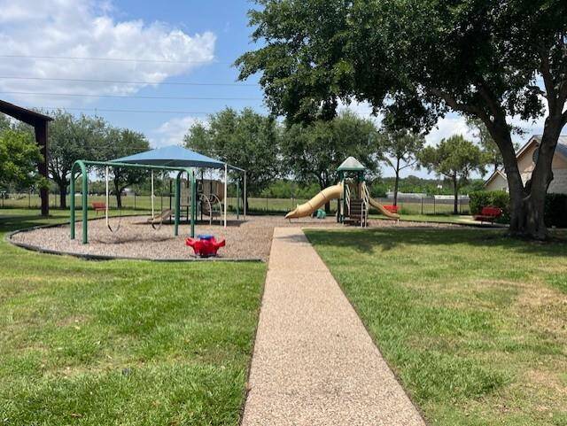 A charming playground area with swings, a slide, and a small climbing structure, set on a well-maintained lawn. It's surrounded by mature trees, providing shade and a welcoming atmosphere for families.