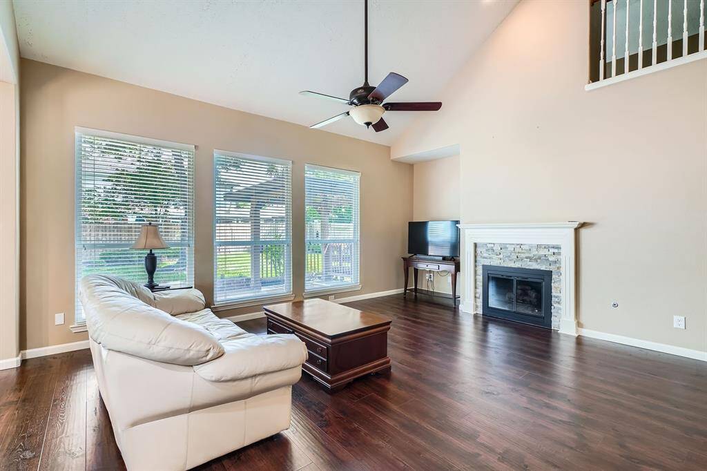 Bright and spacious living room with high ceilings, featuring large windows, and a cozy fireplace. Ideal for family gatherings and relaxation.