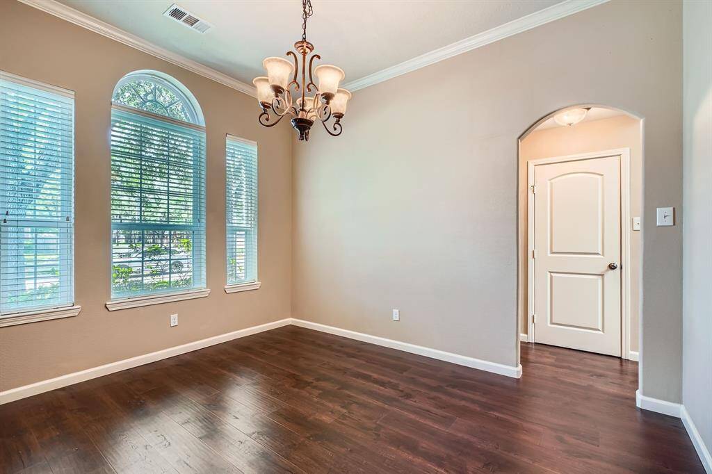 This room features elegant flooring, large windows with ample natural light, and a stylish chandelier. The soft neutral walls and arched doorway add a touch of sophistication, making it ideal for a dining or living area.