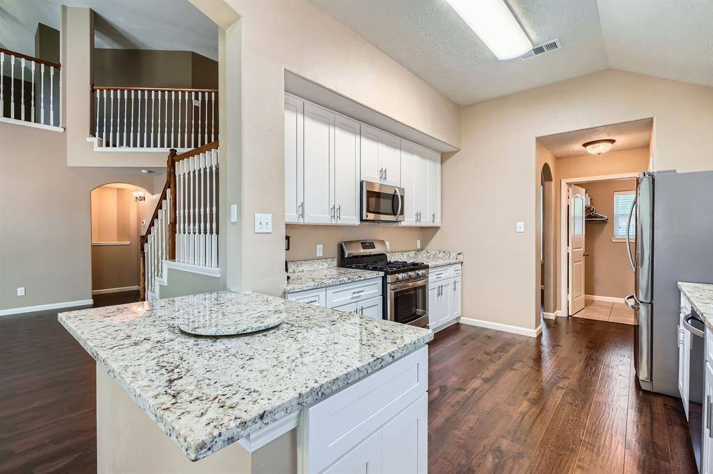 This photo showcases a spacious kitchen with granite countertops, and stainless-steel appliances. It features white cabinetry and an open layout leading to a staircase with elegant railings, enhancing the home's modern and inviting feel.