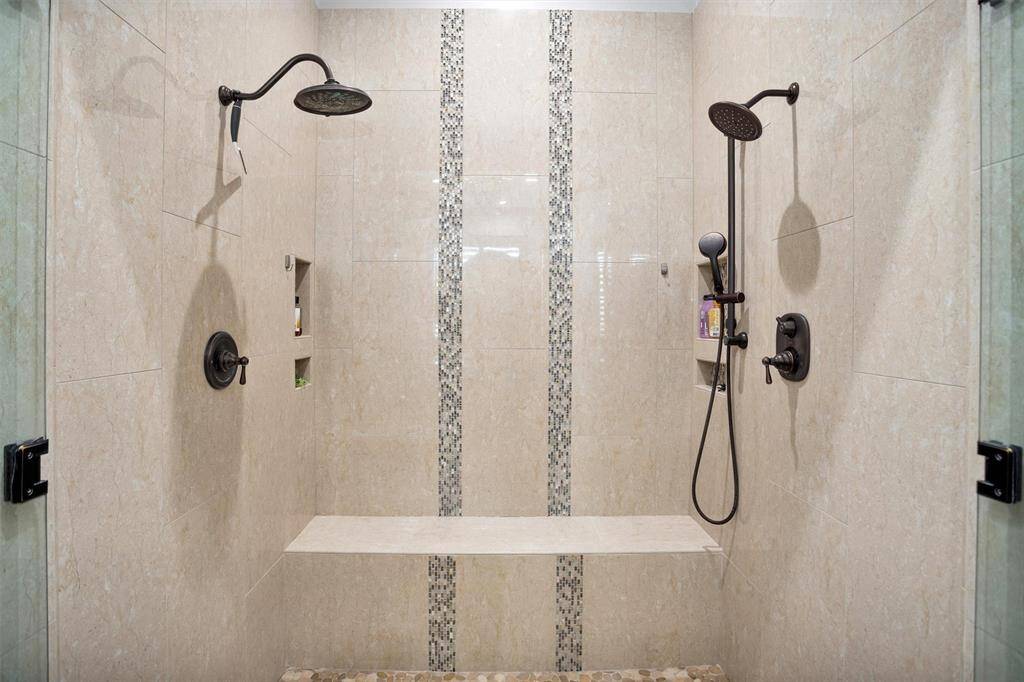 Step into luxury with this oversized walk-in shower, complete with dual shower heads, a built-in bench, and elegant tile accents.