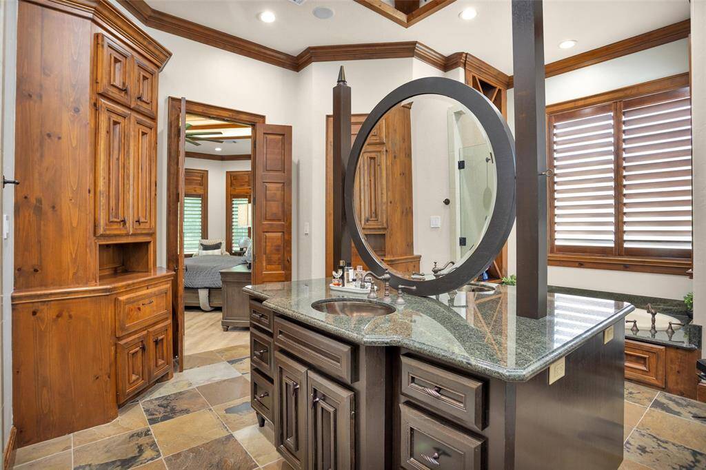 The centerpiece of the primary bathroom is this custom granite island with circular mirror, dual sinks, and rich wood cabinetry—designed for both function and style.