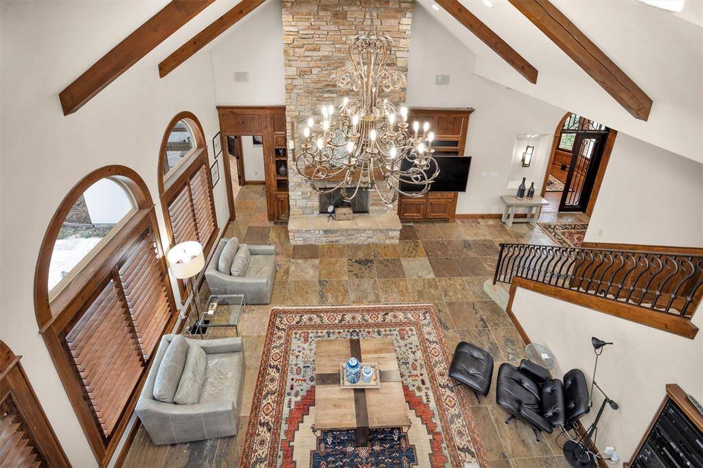 From the upstairs landing, take in the dramatic view of the living room with soaring ceilings, wood beams, a massive chandelier, and stone fireplace.