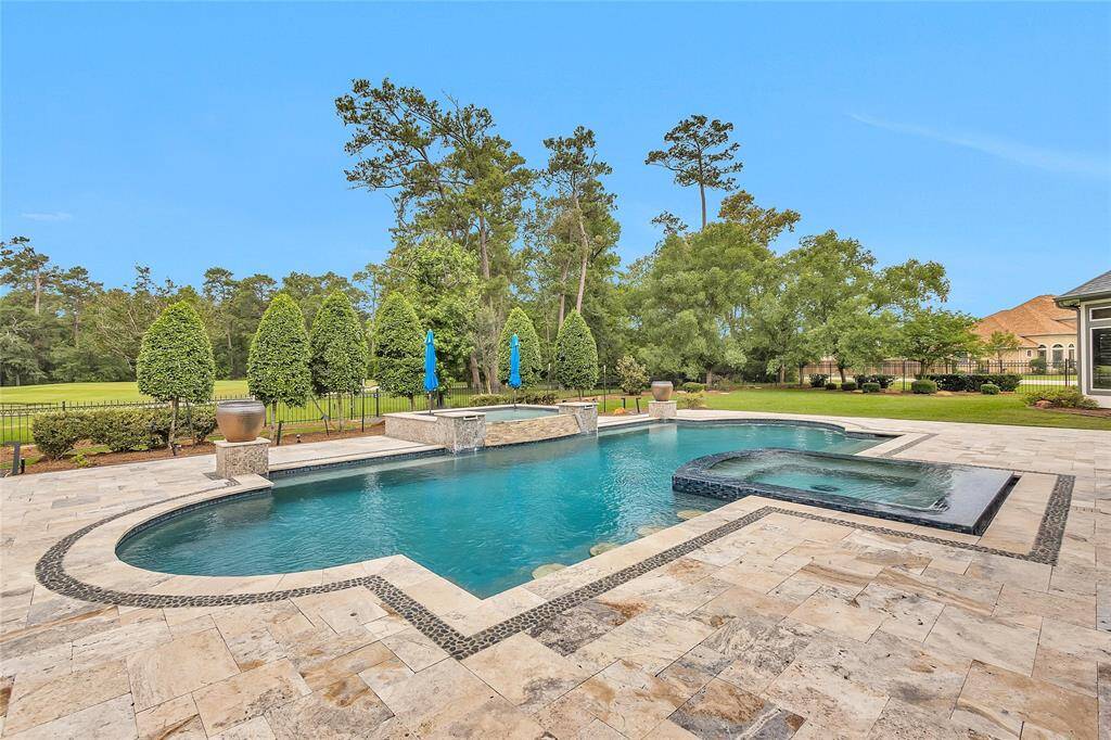 Enjoy serene views and ultimate relaxation from this resort-style pool and spa, featuring elegant pebble inlay accents, a spacious travertine deck, soothing water features, and a backdrop of manicured trees and golf course greens.