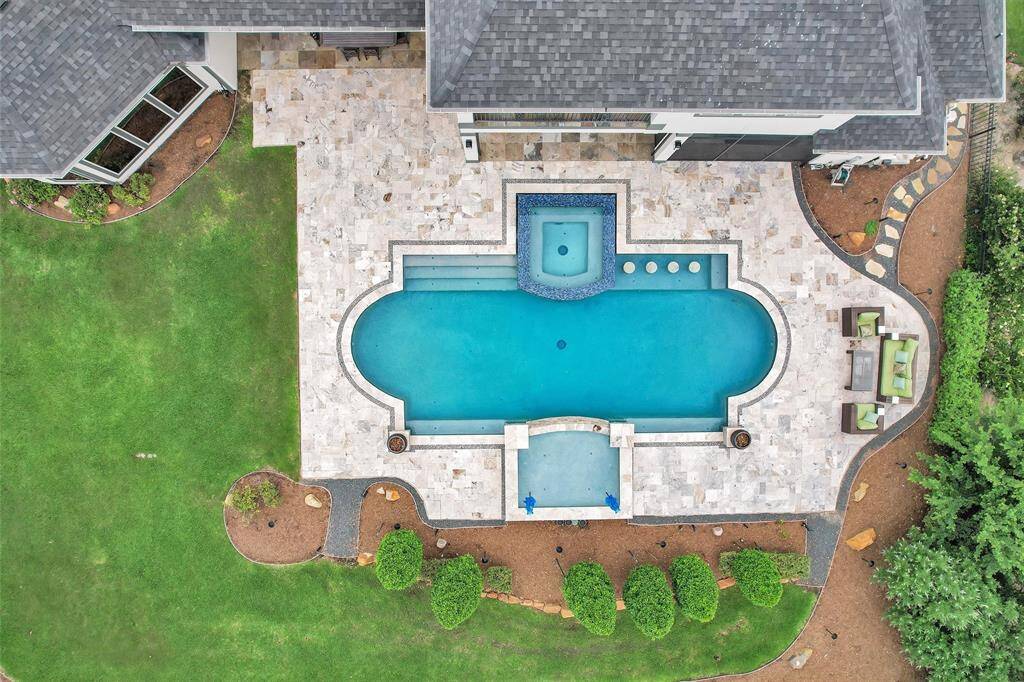 A bird’s eye view reveals the true elegance of this custom-designed backyard, complete with travertine decking, waterfall features, sunken barstools, and lush landscaping.
