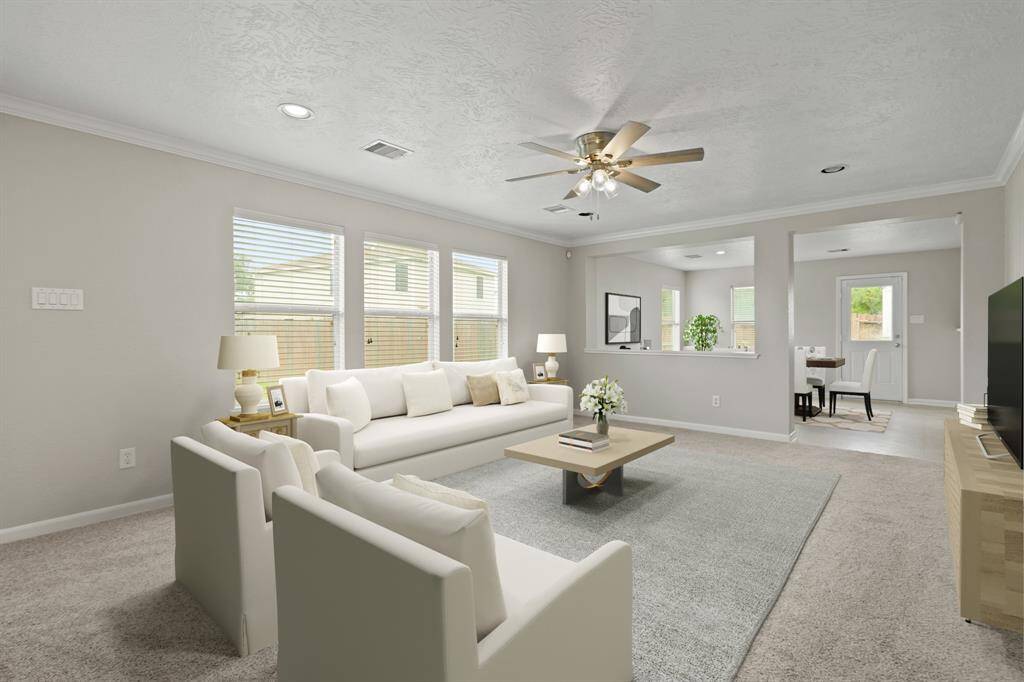 Virtually Staged: This living room is open and bright! It features large windows with privacy blinds, carpet floors, crown molding details, recessed lighting, and a ceiling fan. It flows seamlessly into the dining and kitchen areas.