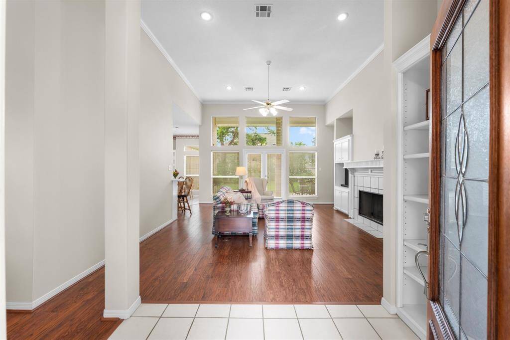 Bright and inviting freshly painted living room with high ceilings, large windows, and wood flooring. Features a cozy fireplace, built-in shelving, and an open layout leading to the dining area. Perfect for relaxation and entertaining.