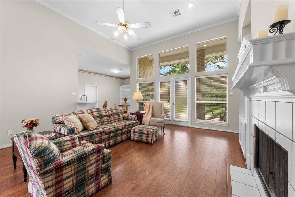 Bright and spacious living room with high ceilings, large windows, and wood flooring. Features a cozy fireplace and access to a patio area, perfect for natural light and entertaining.