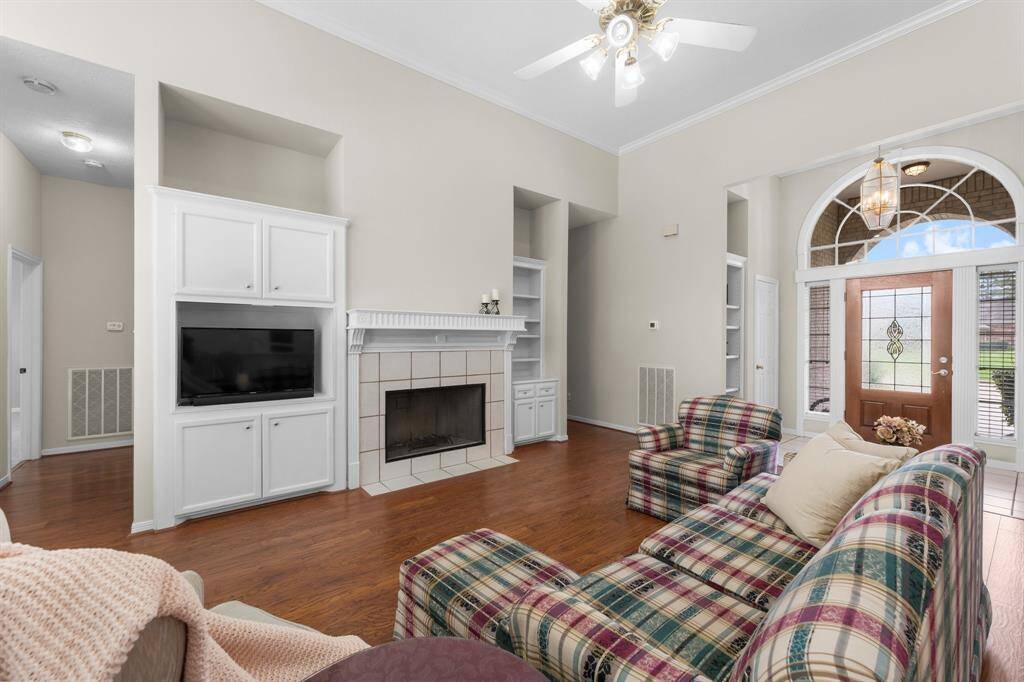 Spacious Freshly Painted living room with high ceilings, featuring a gas log fireplace, built-in shelving, and wooded floors. The large windows by the entrance offer plenty of natural light. A great gathering space in the center of the home!