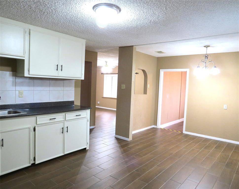 Bright and inviting space with an open floor plan. Features a kitchen area with white cabinetry, tile backsplash, and dark countertops. The room has warm-toned walls, tile flooring, and modern lighting. Ideal for comfortable living and entertaining.