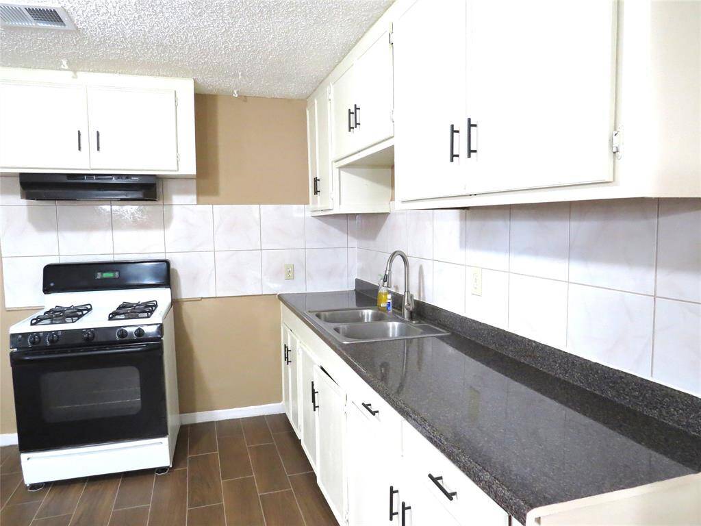 This kitchen features white cabinets, dark countertops, and a gas stove. The space includes a double sink and wood-look tile flooring, offering a clean and functional layout.