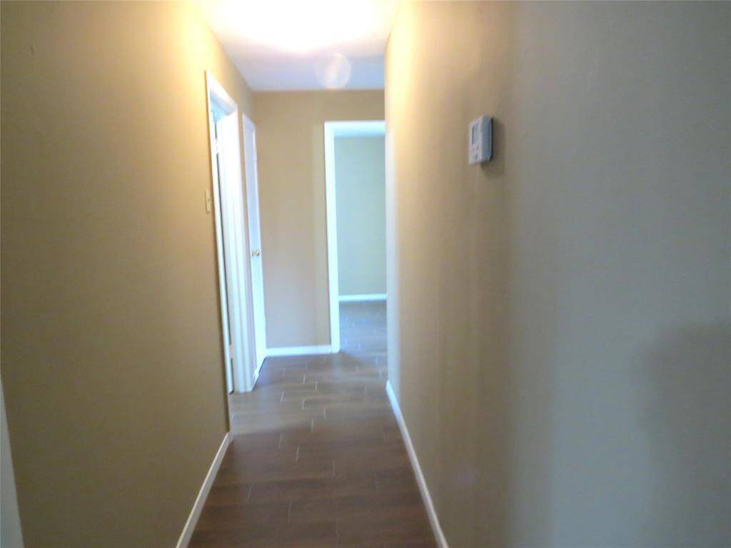 A well-lit hallway with neutral walls leads to multiple rooms. The flooring is a polished wood-like material, adding warmth and elegance.