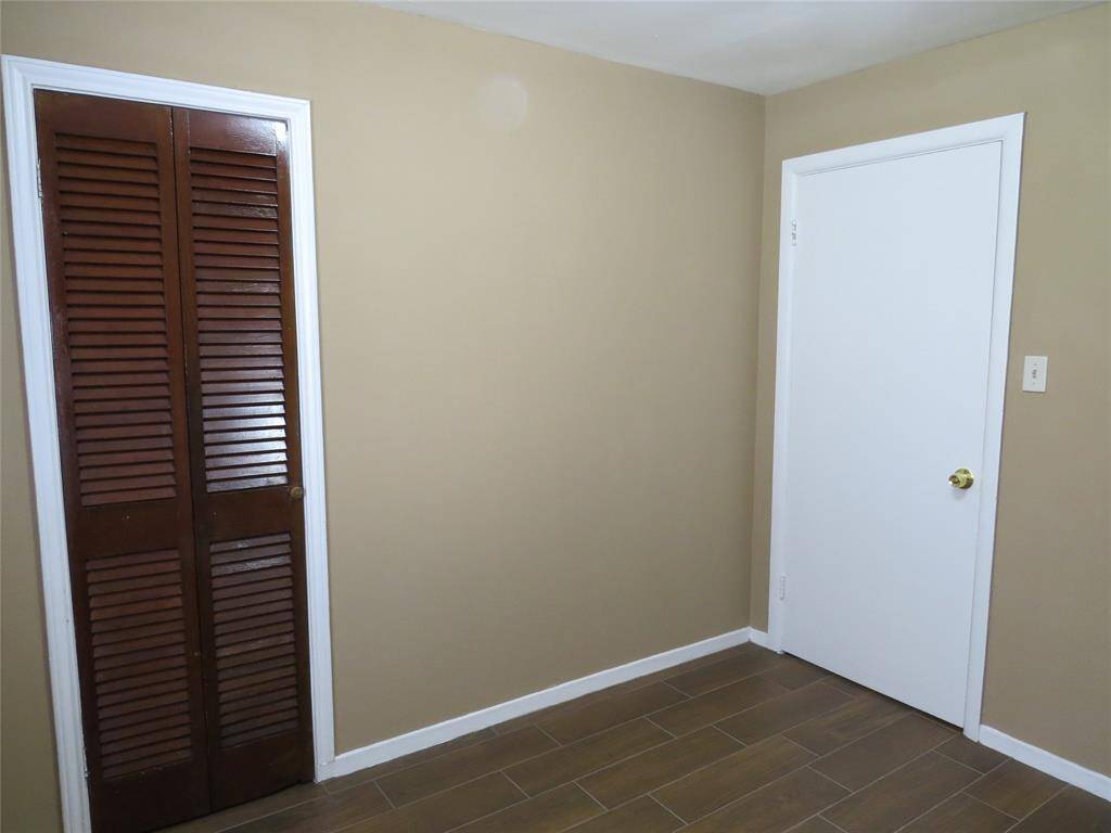 This room features neutral-colored walls, a white door, and a closet with wooden louvered doors. The floor is tiled with a wood-like finish, offering a clean and simple look.
