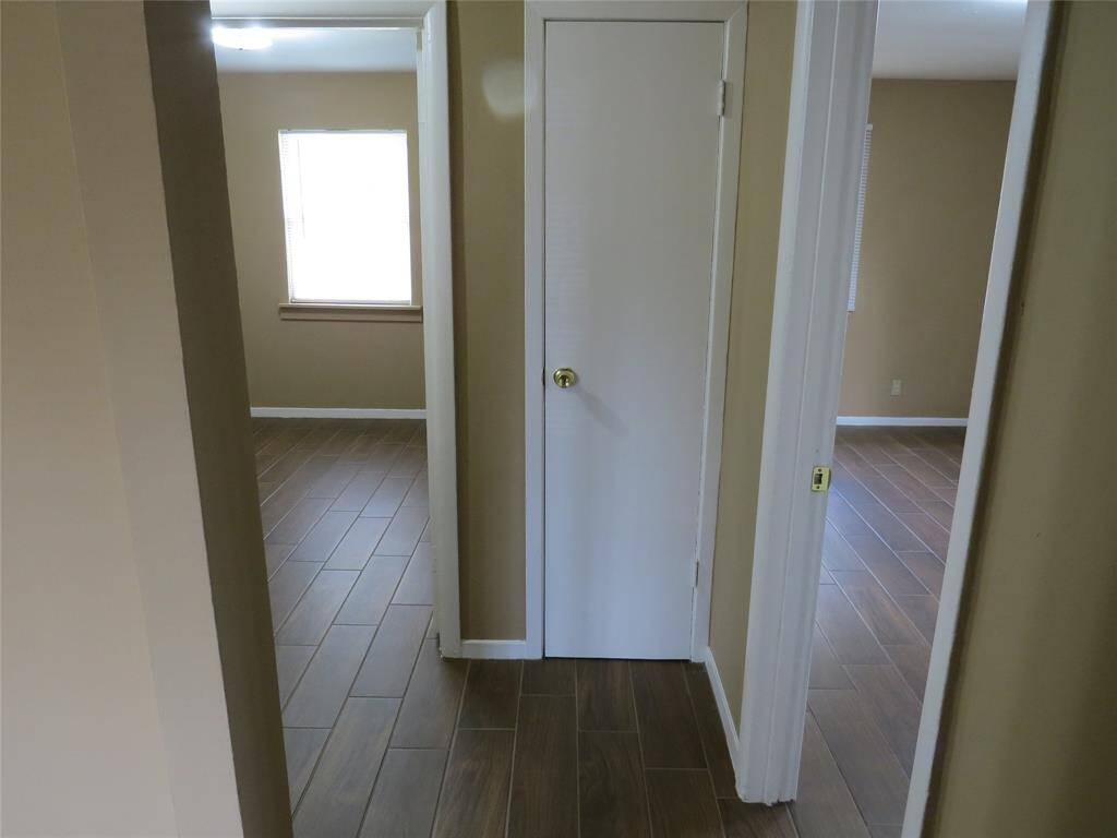 This photo shows a hallway with two rooms on either side, featuring light brown walls and wood-like tile flooring. There are white doors and windows providing natural light.