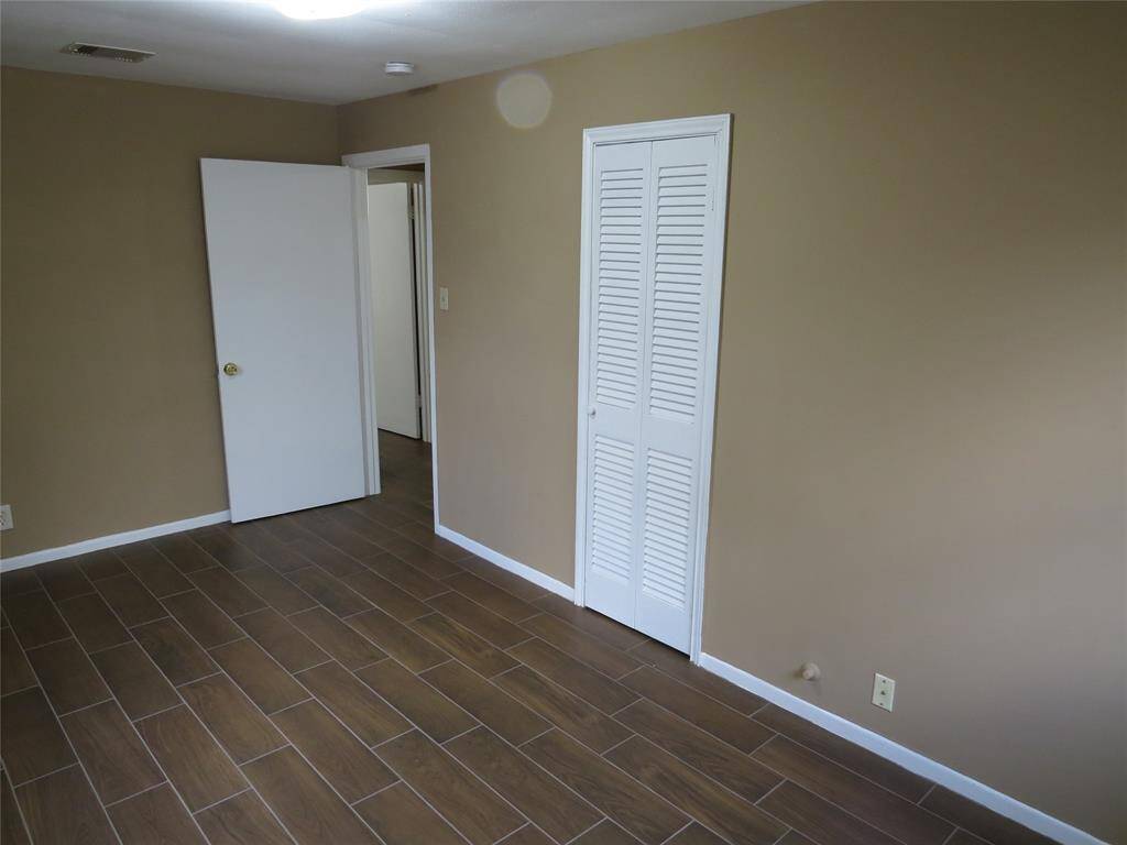 This room features neutral beige walls and wood-look tile flooring, creating a warm and inviting space. It includes a white door and a closet with louvered doors, offering practical storage. Ideal for a bedroom or office.