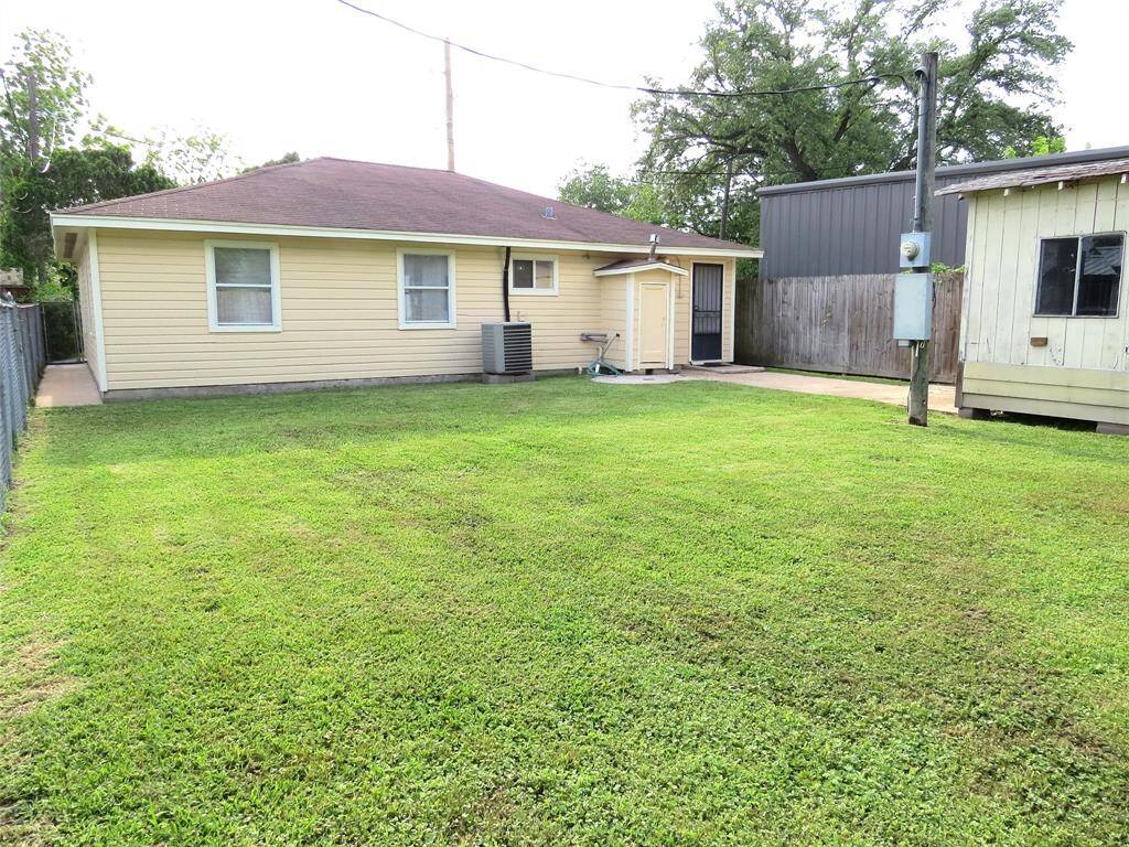 This photo shows a cozy single-story home with a light yellow exterior, a red roof, and a spacious grassy backyard. It features a small paved area and is bordered by a fence, offering privacy and outdoor space.