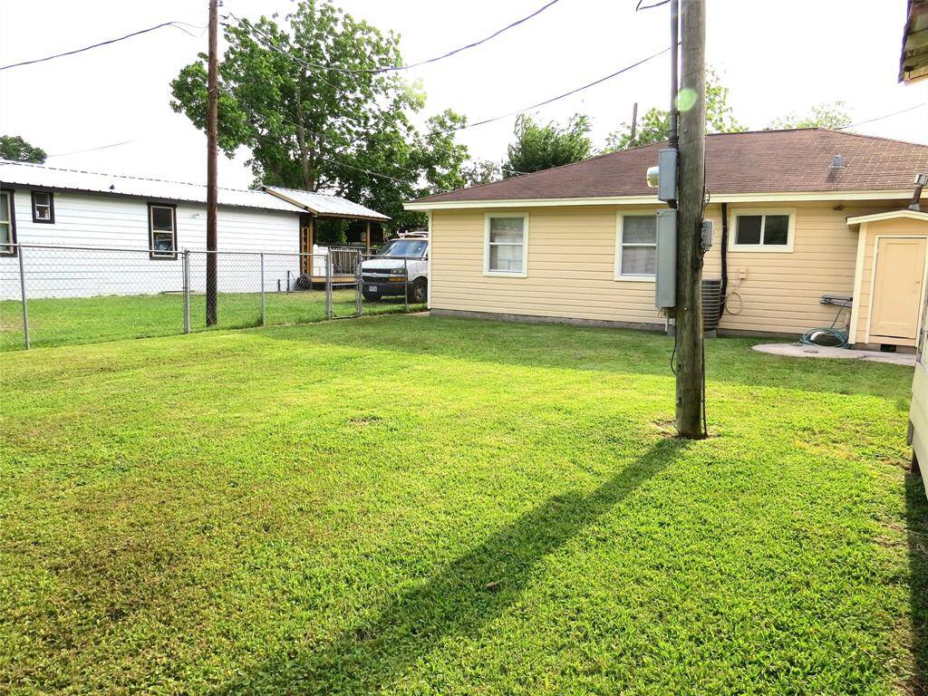 This photo shows a backyard of a single-story home with a well-maintained lawn, a yellow exterior, and a small storage area. The yard is enclosed by a chain-link fence, providing a sense of privacy and security.