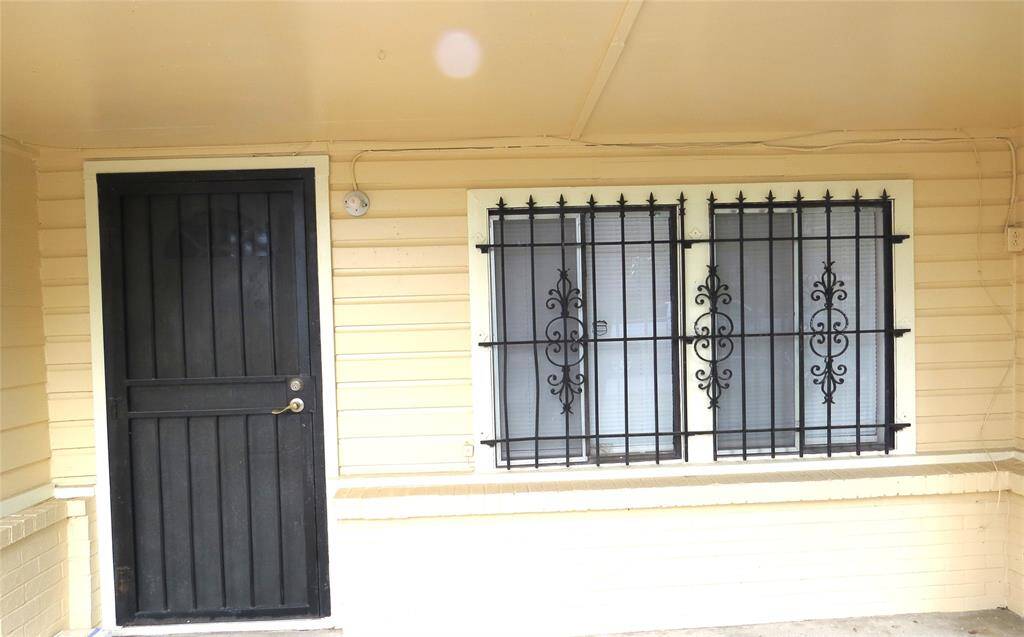 This photo shows a house entrance with a sturdy black door and barred windows for added security. The exterior is painted in a light color, giving it a welcoming look.