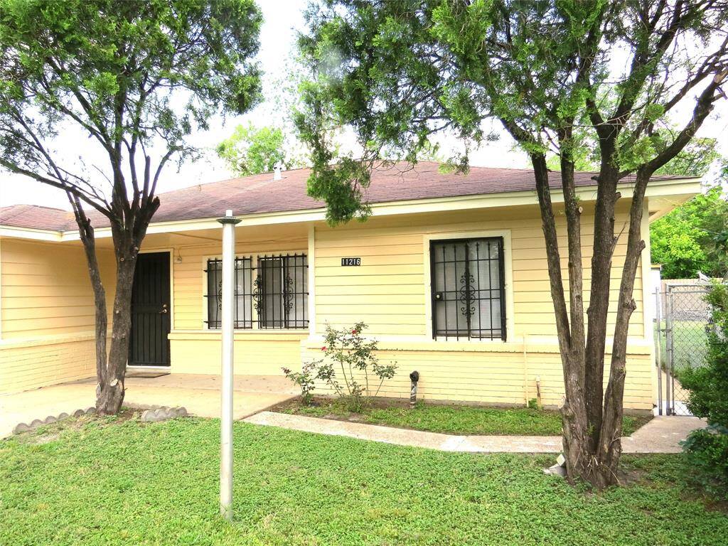 Charming single-story home with a yellow exterior, featuring a secure gated front and mature trees. Ideal for those seeking a cozy, welcoming atmosphere with a touch of nature.