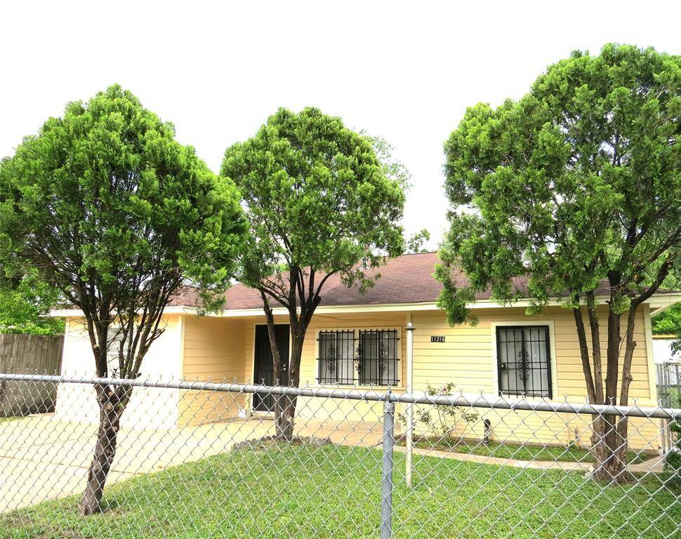 Charming single-story yellow home with a fenced front yard and mature trees. Features a driveway and a welcoming entrance.