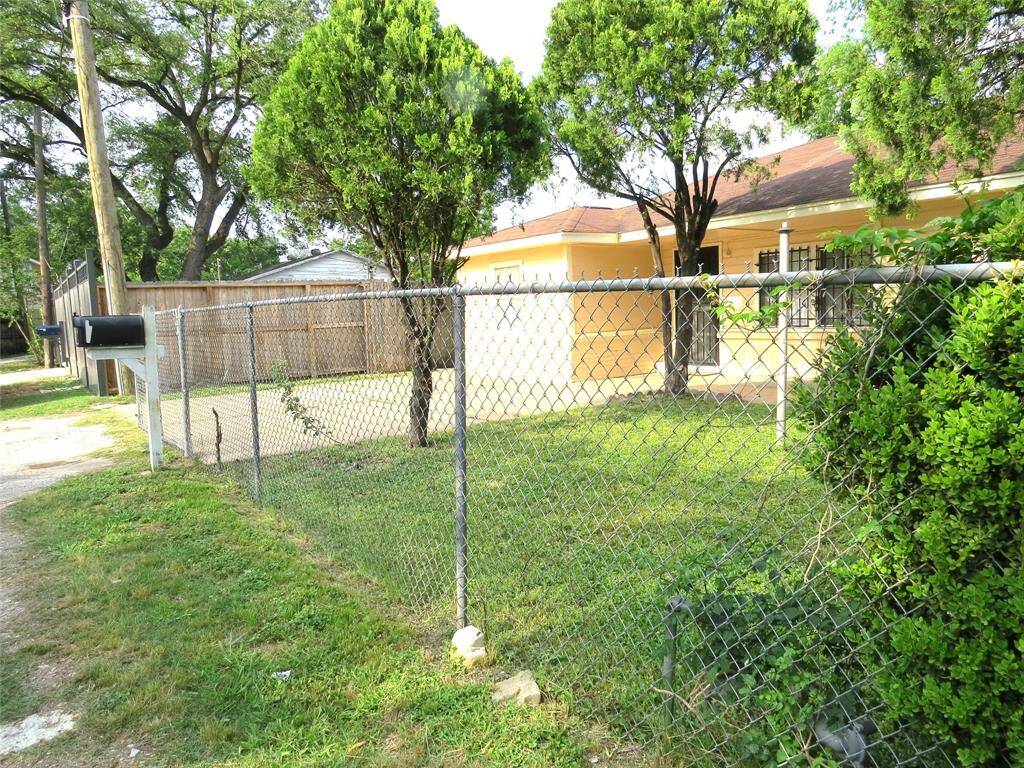 This photo shows a charming home with a yellow exterior, surrounded by a chain-link fence. It features a well-maintained front yard with grassy areas and mature trees, providing both shade and privacy. Perfect for buyers seeking a cozy, inviting property.