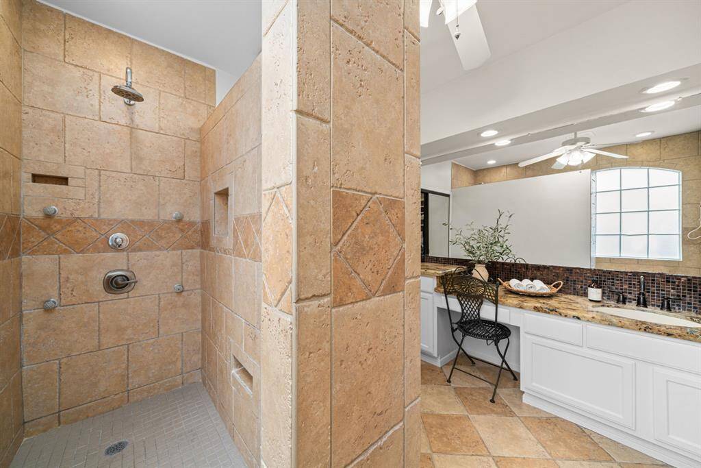 This luxury walk-in shower boasts neutral stone tiles, built-in niches, 4 additional body sprayers, and heated towel rack.